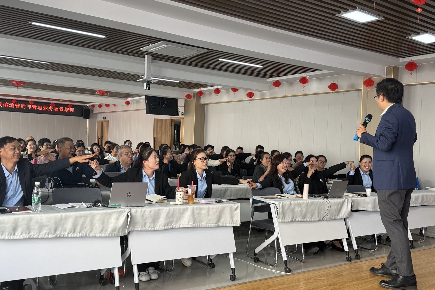 平罗县中小企业公共服务中心 AI 办公提效课，学员举手互动，讲师持麦在台前